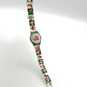 May include: A vintage wristwatch with a green face and band. The watch face features a red elephant design. The band is decorated with various colorful animal and plant illustrations. The watch is a unique accessory.