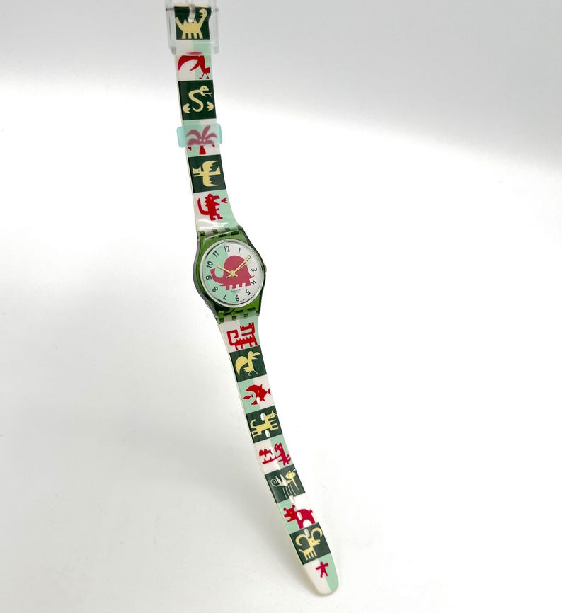 May include: A vintage wristwatch with a green face and band. The watch face features a red elephant design. The band is decorated with various colorful animal and plant illustrations. The watch is a unique accessory.