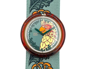 May include: A Swatch watch with a parrot design on the face. The watch has a brown case and a teal strap with a repeating floral pattern. The watch face features a parrot in yellow, orange, and green.