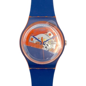 May include: A blue Swatch watch with an orange inner dial and a clear face. The watch has a blue silicone strap. The watch face displays the inner workings of the watch. The watch is labeled "Swatch Swiss".