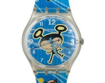 Peut inclure: Une montre Swatch bleue et blanche avec un boîtier en plastique transparent. Le cadran de la montre présente un personnage de dessin animé avec des cheveux noirs et des oreilles jaunes. Le bracelet de la montre a un motif bleu et blanc avec un vaisseau spatial de dessin animé et un cheval de dessin animé.