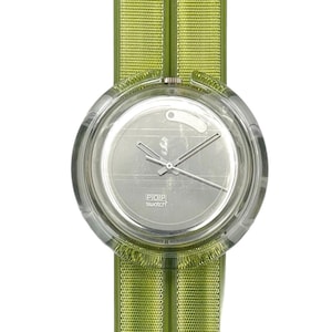 Puede incluir: Un reloj Swatch Pop transparente con esfera plateada y agujas plateadas. El reloj tiene una correa de tela verde lima. La esfera del reloj tiene el texto "POP Swatch".