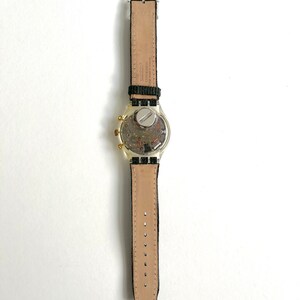 May include: A silver and gold wristwatch with a black leather band. The watch face is visible and has a chronograph function.