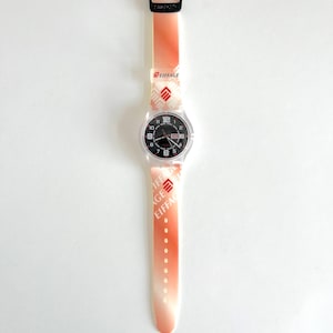 Puede incluir: Un reloj Swatch blanco y naranja con una esfera negra y un logotipo "Eiffage" rojo en la correa.
