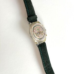 May include: A silver and white wristwatch with a black and green corduroy band. The watch face has a white background with black and red numbers and hands. The watch face also has three smaller dials with black and white numbers.