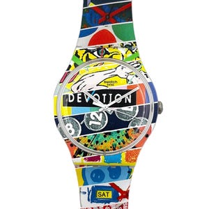 Op de afbeelding: Een kleurrijk Swatch-horloge met een patroonband. De wijzerplaat toont het woord "DEVOTION" en het nummer "12". De band heeft een verscheidenheid aan kleuren en ontwerpen, waaronder het woord "SAT".