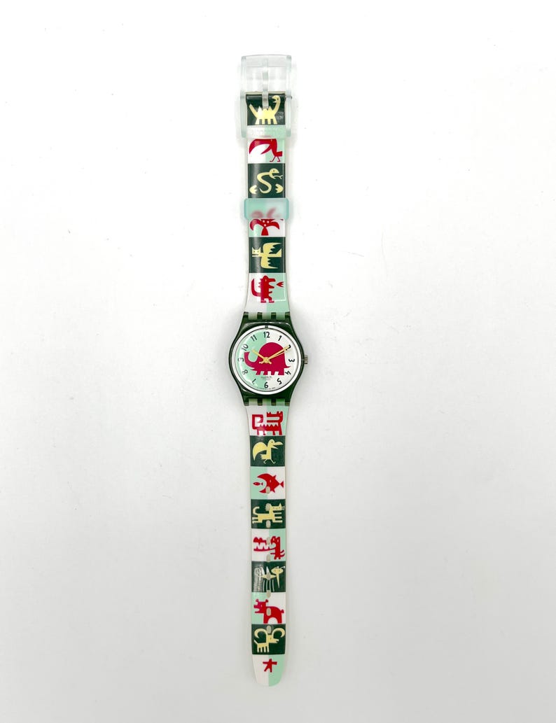 May include: A vintage wristwatch with a white face, black numbers, and red hands. The watch band is light green with red and yellow animal graphics. The watch case is dark green. The watch is a unique accessory.