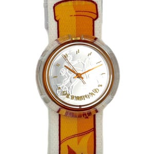 Puede incluir: Un reloj de pulsera transparente con una esfera plateada que presenta una figura clásica y la palabra "OLYMPIAD" en oro. El reloj tiene agujas doradas y una correa blanca con un diseño de llama amarilla y naranja.