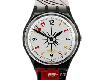 Peut inclure: Une montre Swatch blanche et noire avec une aiguille des secondes rouge. Le cadran de la montre présente un motif d'étoile noire et des chiffres romains noirs pour les heures. Le bracelet de la montre est noir avec un imprimé graphique coloré d'une scène de ville. Le texte "Swatch Swiss" et "SWATCH AQ 1995" est imprimé sur le cadran de la montre. Le texte "P9-13" et "TAXI" est imprimé sur le bracelet de la montre.