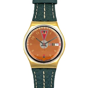 Puede incluir: Un reloj de pulsera dorado con esfera marrón, manecillas negras y visualización de la fecha. Tiene una correa de cuero verde oscuro con costuras blancas. La esfera incluye un diseño de triángulo rojo y negro y la palabra "watch".