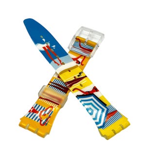 May include: A colorful watch strap with a beach theme. The strap features illustrations of a surfer, beach umbrellas, and striped patterns in blue, yellow, and red. The buckle is clear plastic.