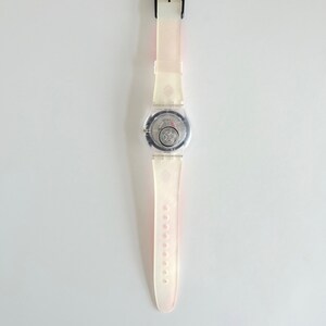 Puede incluir: Un reloj de pulsera de pl&aacute;stico blanco con una esfera transparente y una hebilla negra. El reloj tiene una correa blanca con una franja rosa.