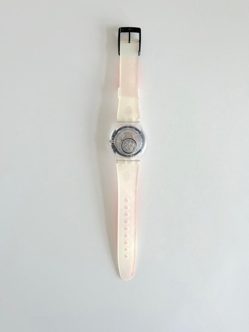 Puede incluir: Un reloj de pulsera de pl&aacute;stico blanco con una esfera transparente y una hebilla negra. El reloj tiene una correa blanca con una franja rosa.