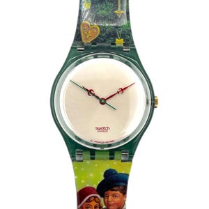 Op de afbeelding: Een Swatch horloge met een groene band en een witte wijzerplaat. De wijzerplaat heeft rode en groene wijzers. De band heeft een kerstboomontwerp en een afbeelding van twee kinderen. Het horloge is gemarkeerd met "Swatch Swiss AG 1995".