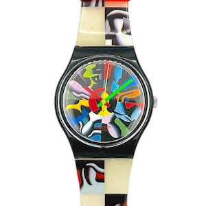 Op de afbeelding: Een vintage Swatch horloge met een zwarte kast en een kleurrijk abstract ontwerp op de wijzerplaat. De horlogeband is een mix van zwart, wit en rood. De wijzers van het horloge zijn groen en rood.