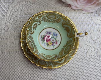 Peut inclure: Une tasse à thé et une soucoupe vintage avec un motif floral délicat et une bordure dorée. La tasse et la soucoupe sont de couleur vert pâle avec un centre blanc orné d'un bouquet de fleurs.