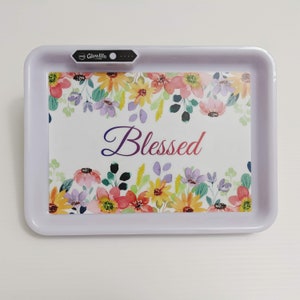 May include: White rectangular tray with a floral design and the word "Blessed" in a colorful font. The tray has a small black device with the word "Glowlife" on it.