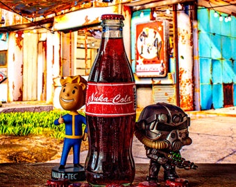 May include: A brown glass bottle with a red label that says "Nuka-Cola" and a red cap. The bottle is sitting on a table with a small figurine of a character from the Fallout video game series and a small robot figurine.