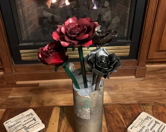 May include: A bouquet of four metal roses in a silver vase. The roses are red, black, and silver. The vase is sitting on a wooden table.