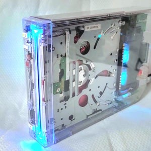May include: A clear, transparent Nintendo Wii console with blue LED lights. The console is open, revealing the internal components.