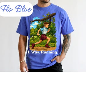 May include: A Flo Blue short-sleeve t-shirt featuring a graphic illustration of a person running through a green forest. The person wears a blue plaid shirt and maroon shorts. Below the illustration, the text reads, I. Was. Running.