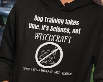 May include: Black hoodie with white text that reads "Dog Training takes time. It's Science, not WITCHCRAFT" with a crossed-out image of a skull and bones. The text below the image reads "SPELLS & HEXES WOULD BE NICE, THOUGH"