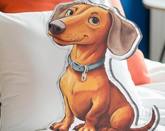 Puede incluir: Un cojín decorativo con forma de perro salchicha de dibujos animados. El perro es marrón con un collar azul claro y una expresión sonriente. El cojín está sobre una almohada blanca con cojines naranjas y estampados en el fondo.