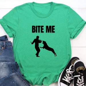 May include: A green t-shirt with the text "BITE ME" in black. A silhouette of a person and a dog are below the text.