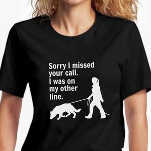 May include: Black t-shirt with white text that reads "Sorry I missed your call. I was on my other line."  A white silhouette of a person walking a dog is below the text.