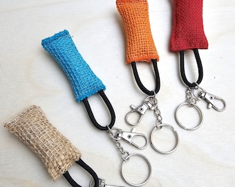 Könnte beinhalten: Vier Schlüsselanhänger mit verschiedenen farbigen Stoffbeuteln, die an silbernen Schlüsselringen befestigt sind. Die Beutel sind aus Jute und in den Farben Orange, Rot, Blau und Natur.