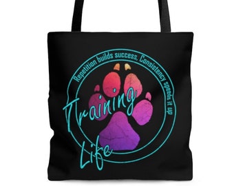 May include: Black tote bag with a turquoise circle and the text "Training Life" inside. The circle has a pink, purple, and orange paw print inside. The text "Repetition builds success. Consistency speeds it up" is written around the circle.