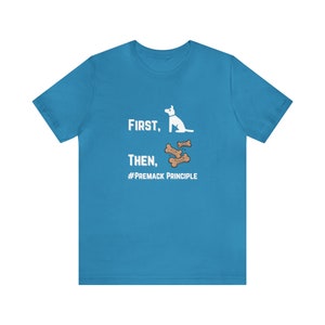 Puede incluir: Camiseta turquesa con el texto "First, Then, #Premack Principle" y un gráfico de un perro blanco y huesos. La camiseta está hecha de un material suave.