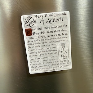 May include: A white ceramic mug with a black handle and the text "But First, Coffee" in a handwritten style. The mug is on a white surface. The mug is 10 cm tall.