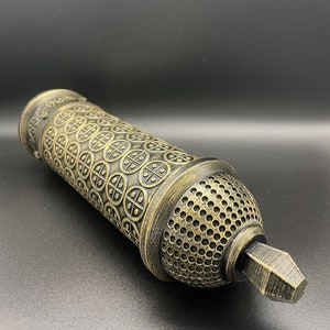May include: A gold and black decorative cylinder with a patterned design. The cylinder has a small, pointed tip at one end.