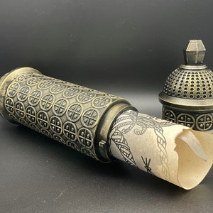 May include: A decorative, ornate, gold-colored metal box with a scroll inside. The box has a detailed design of repeating circles and a domed lid.