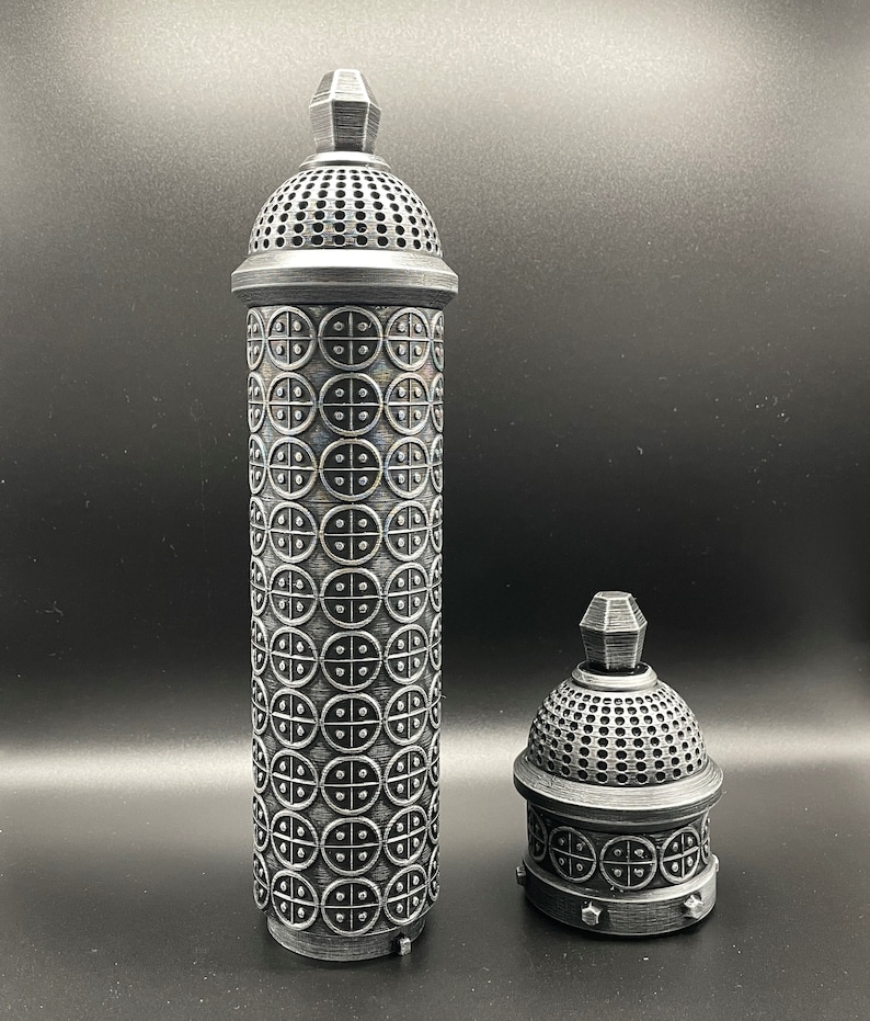 May include: Two silver metal containers with intricate designs. The larger container is taller and has a domed top with a circular pattern. The smaller container is shorter and has a similar domed top with a circular pattern.