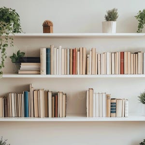May include: White bookshelf with three shelves filled with books and potted plants. The top shelf has a small decorative object on the left side. The middle shelf is filled with books, and the bottom shelf has a few books on the left side and a potted plant on the right side.