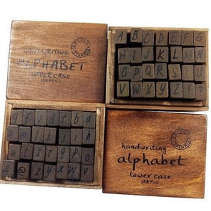 May include: Wooden box set of alphabet stamps, featuring both upper and lower case letters. The stamps are in a vintage style with a handwritten font. The box is labeled "handwriting alphabet" and includes the number of pieces in each case.
