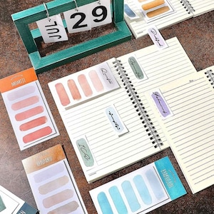 Peut inclure: Un ensemble de notes adhésives aquarelle colorées avec différents motifs et textes. Les notes sont disposées sur un carnet à spirales. Les notes sont parfaites pour ajouter une touche de couleur et de personnalité à votre agenda, journal ou carnet.