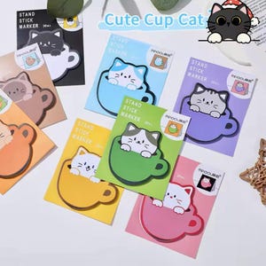 May include: A set of 8 colorful sticky note pads featuring cute cartoon cats peeking out of mugs. Each pad has the text "Stand Stick Marker" and a number.