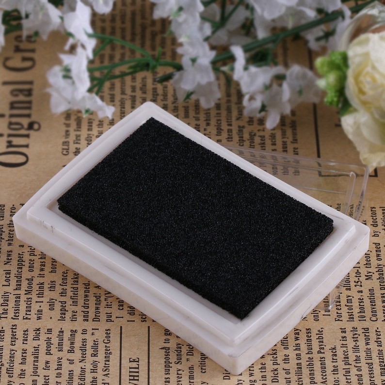 May include: A white ink pad with a black sponge insert. The ink pad is a rectangular shape and is made of plastic.