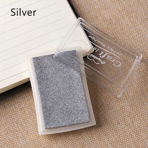 May include: A silver ink pad with a clear plastic case. The case has the text "Craft" and "Embossed" on it.