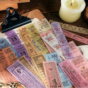 Pu&ograve; includere: Una collezione di adesivi per biglietti in stile vintage in vari colori, tra cui rosa, viola, blu e giallo. Gli adesivi presentano numeri, lettere e parole come "Ryedale Motors" e "Trasporti Pubblici".