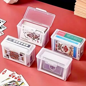 Puede incluir: Cuatro cajas de pl&aacute;stico transparente con tapas que contienen diferentes barajas de cartas. Las cajas est&aacute;n sobre una superficie roja. Las cartas en las cajas incluyen una baraja de cartas est&aacute;ndar, una baraja de cartas de joker, una baraja de cartas chinas y una baraja de cartas con un dise&ntilde;o morado.