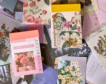 May include: A collection of colourful floral patterned paper cards and notepads. The cards feature various floral designs, including roses, daisies, and other wildflowers. The notepads have a yellow and pink cover with the words "Wanderlust" and "Golden Sunshine" printed on them.