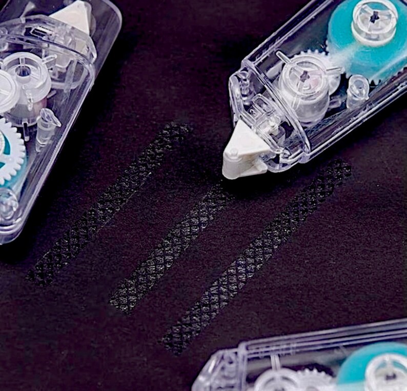 May include: Three clear plastic tape dispensers with blue and white gears. The dispensers are on a black surface with three lines of tape.