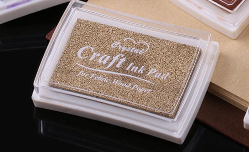 K&ouml;nnte beinhalten: Ein wei&szlig;es Stempelkissen aus Kunststoff mit einem durchsichtigen Deckel. Das Stempelkissen ist mit "Crystal Craft Ink Pad for Fabric, Wood, Paper" beschriftet.
