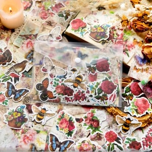 May include: A clear plastic bag filled with colorful vintage-style stickers featuring butterflies, bees, and floral designs. The stickers are on a background of old paper with faded text and images.