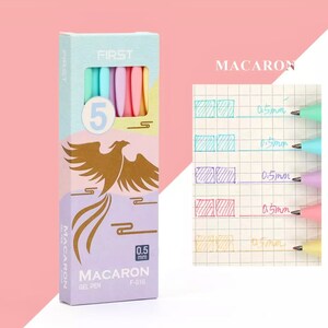 Może przedstawiać: Opakowanie pięciu pastelowych długopis&oacute;w żelowych z motywem złotego feniksa na przodzie. Opakowanie jest oznaczone jako "MACARON" i "FIRST", a długopisy mają grubość 0,5 mm.
