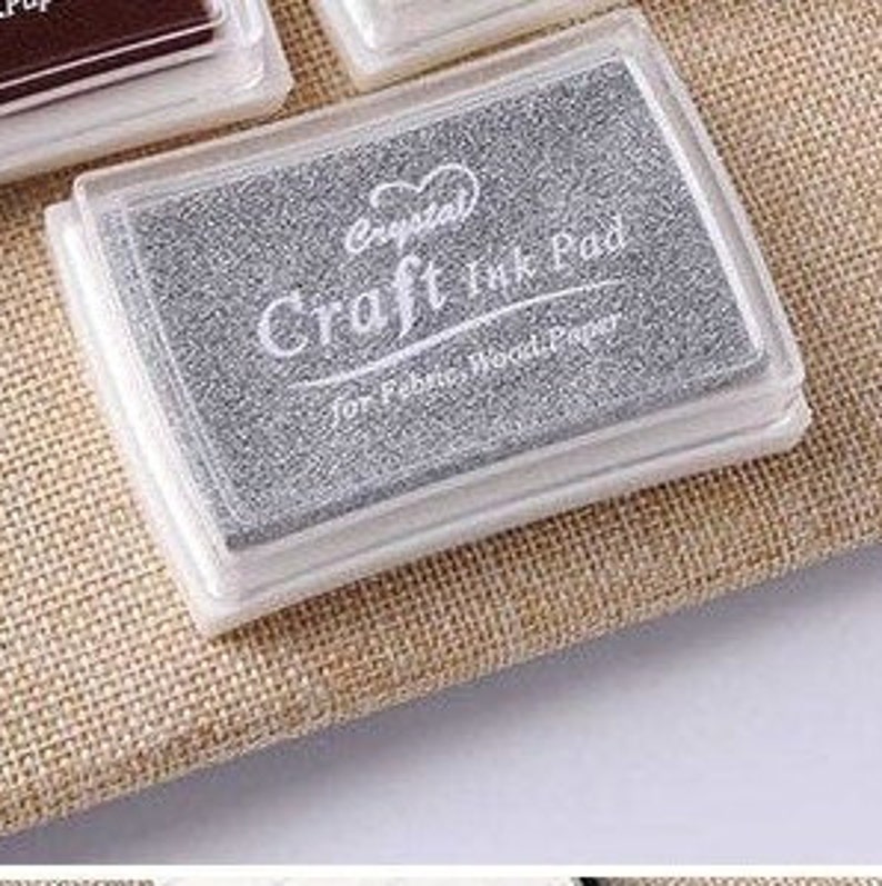 May include: A silver craft ink pad with a clear plastic case. The ink pad is labeled "Crystal Craft Ink Pad for Fabric, Wood, Paper".